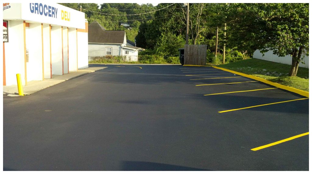 A newly paved commercial parking lot with bright yellow striping beside a grocery and deli building.