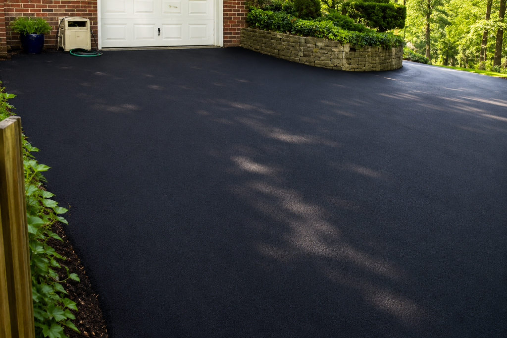A freshly paved residential driveway leading to a garage and stone retaining wall.