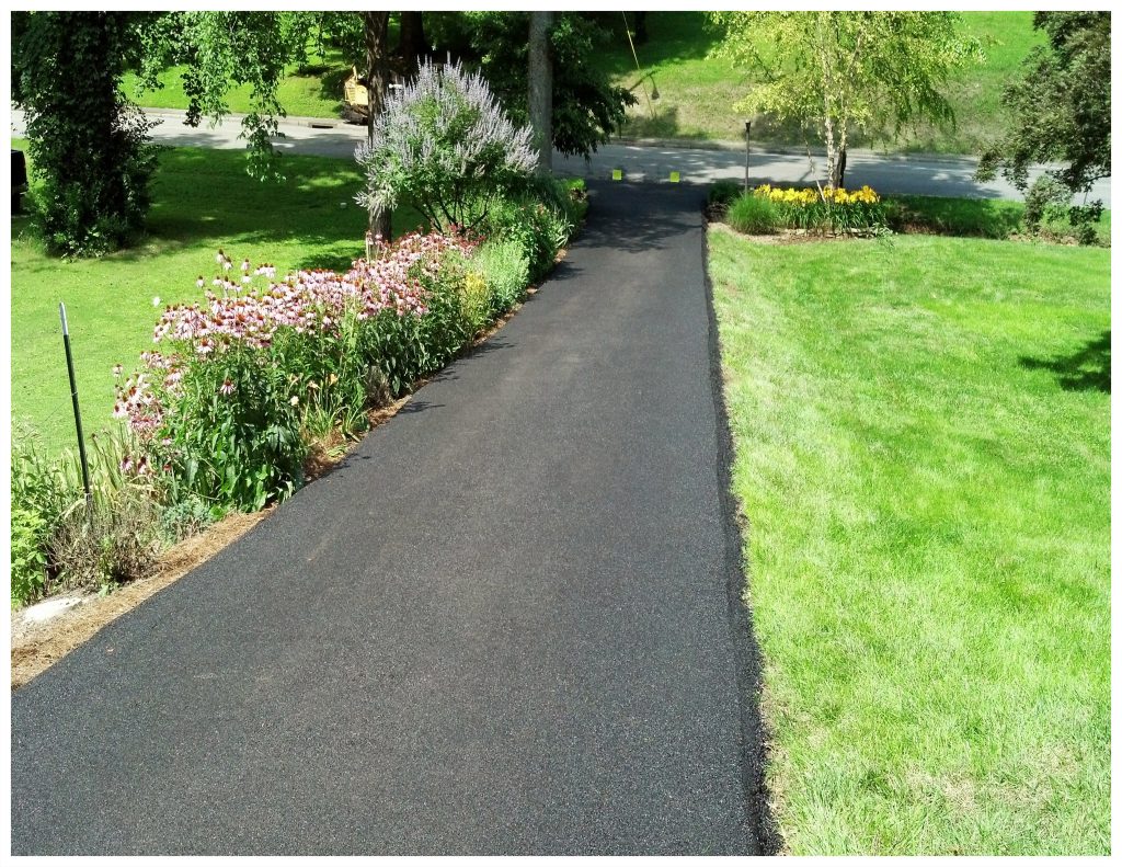 A close view of a smooth finished asphalt driveway beside grass and steps.
